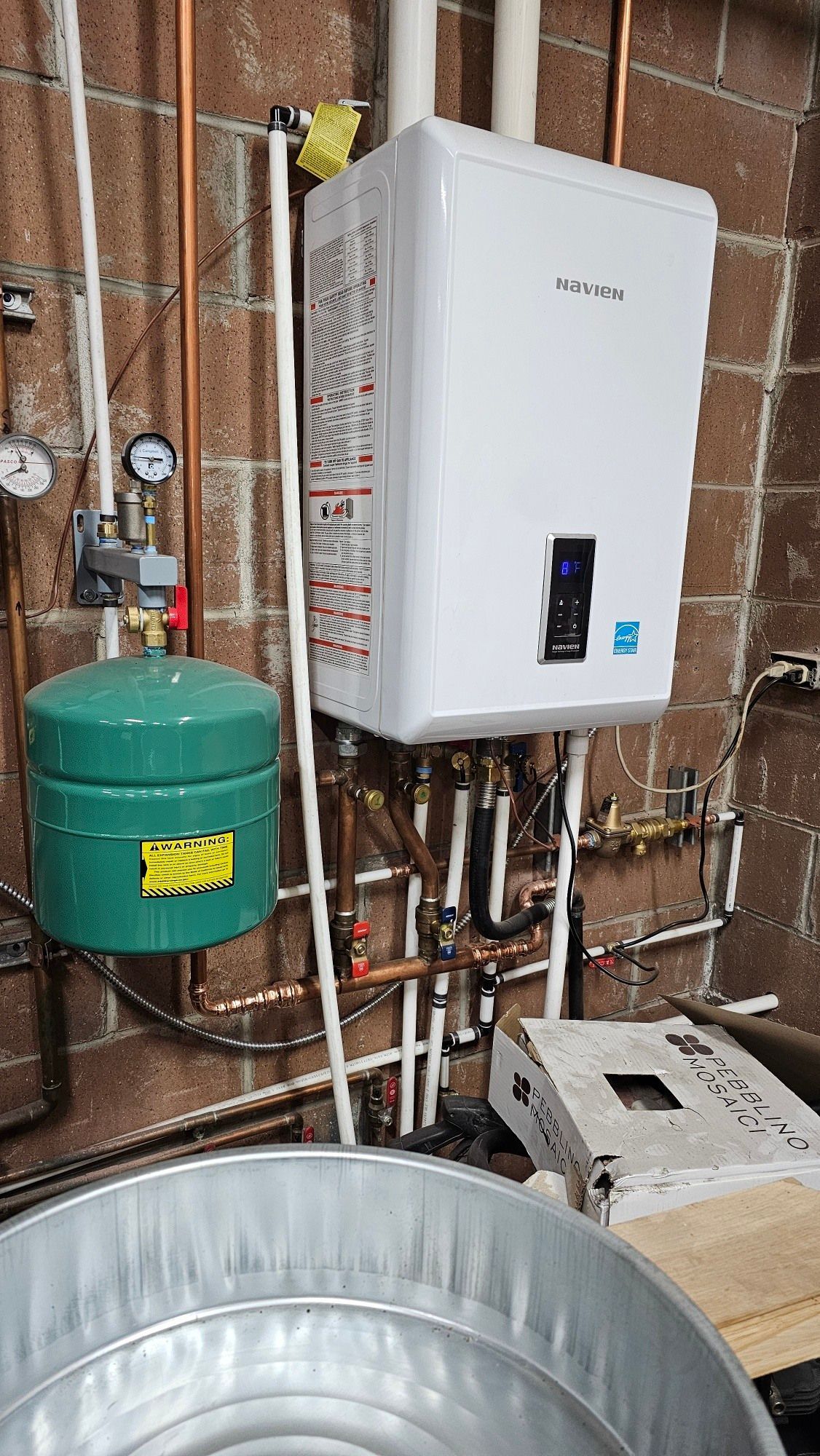 A water heater is hanging on a brick wall next to a green tank.