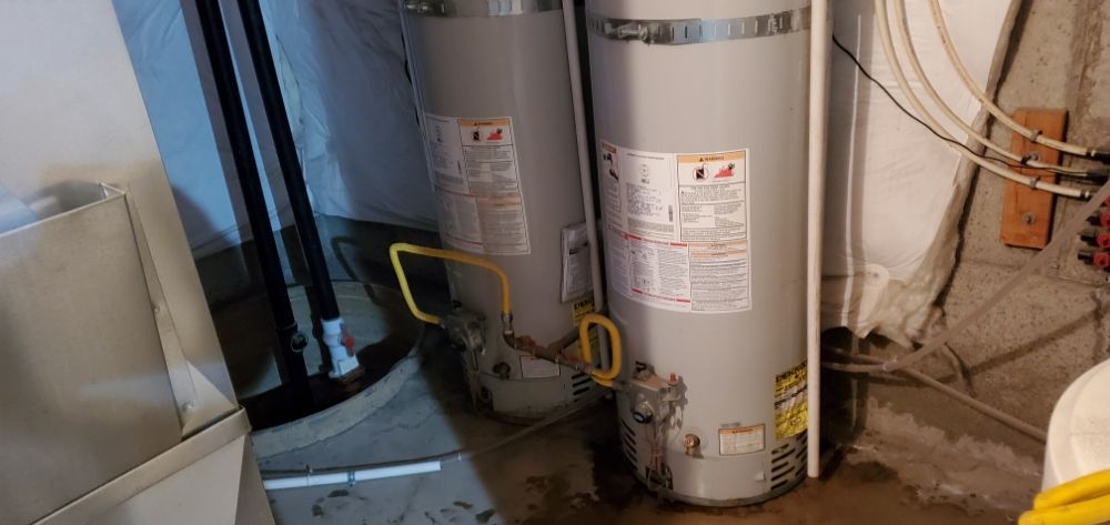Two water heaters are sitting next to each other in a basement.