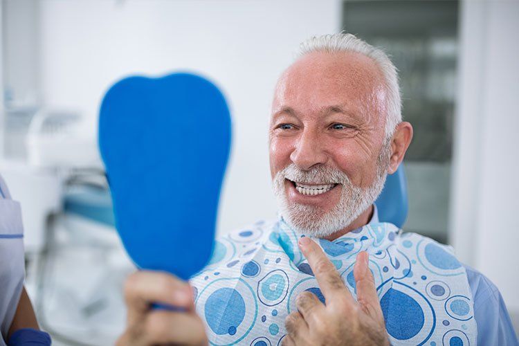 Smiling man in patterned bib holding a blue hand mirror at a dental appointment