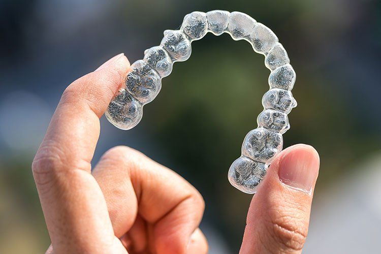 Hands holding a clear dental aligner against a blurred green background