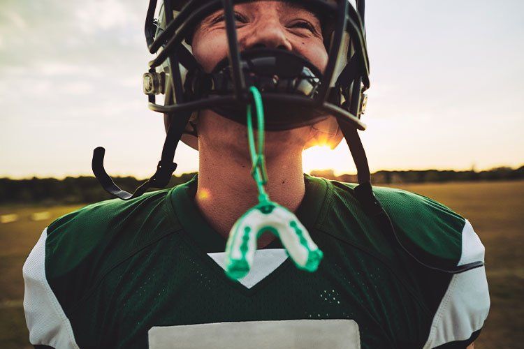 Football player in green jersey and helmet smiling with mouthguard at sunset
