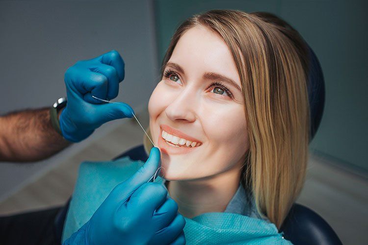 Dentist adjusting a smiling patient’s teeth with blue-gloved hands in a clinic chair