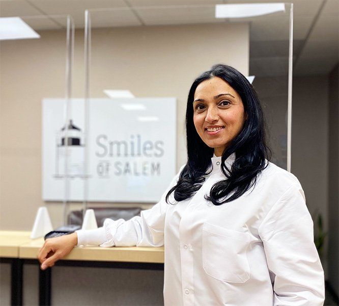 Woman standing at a dental office reception desk with a smile and white coat