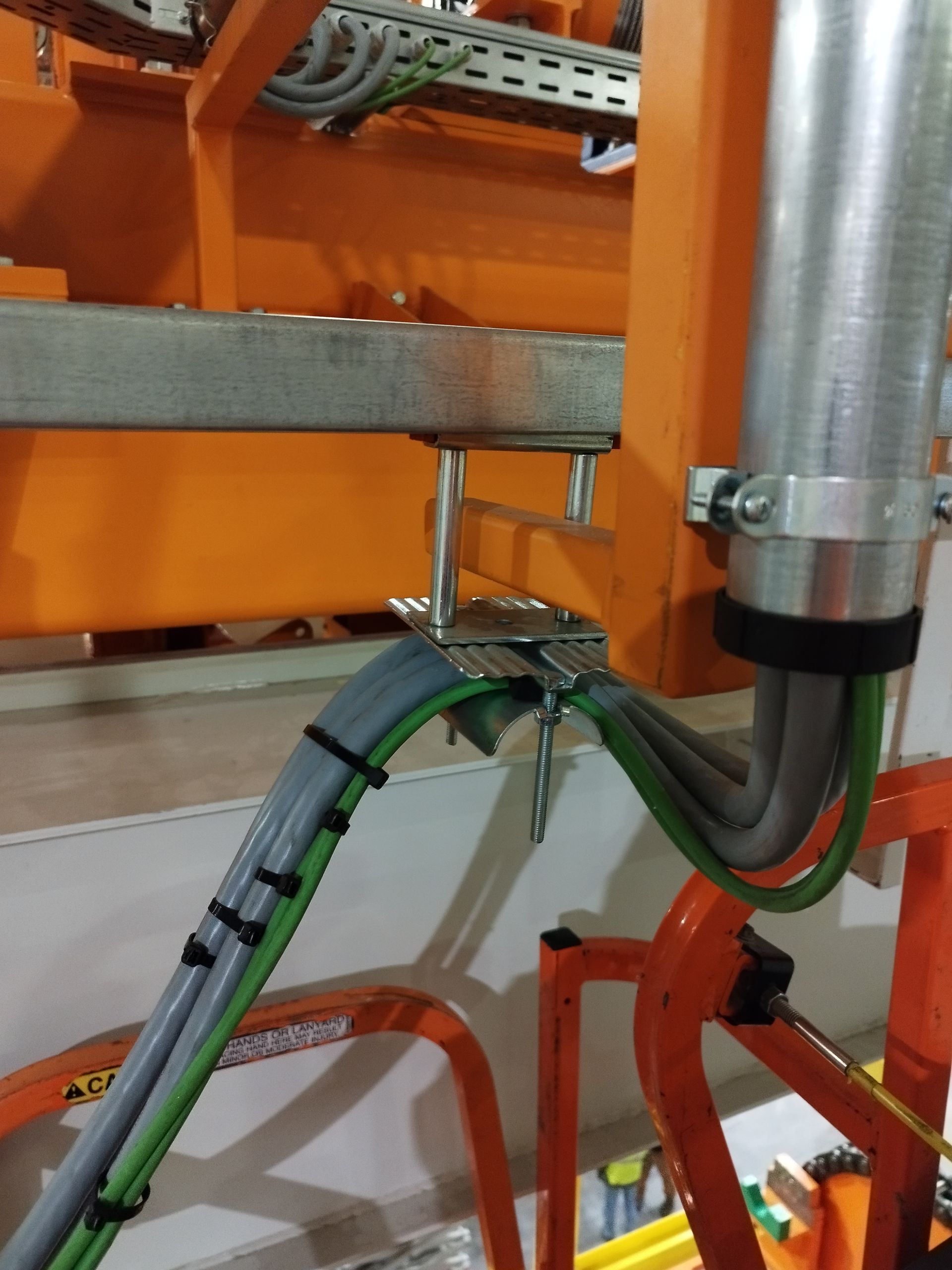 Primo piano del cablaggio elettrico industriale, fissato con clip e staffe metalliche, fissato a travi di supporto arancioni.