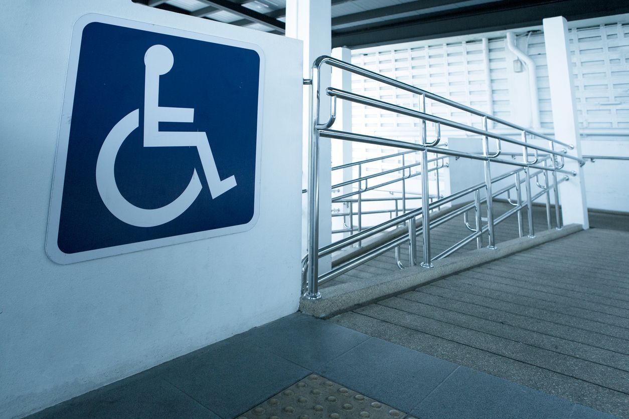Un panneau bleu pour personnes handicapées, une rampe d'accès pour fauteuils roulants avec garde-corps
