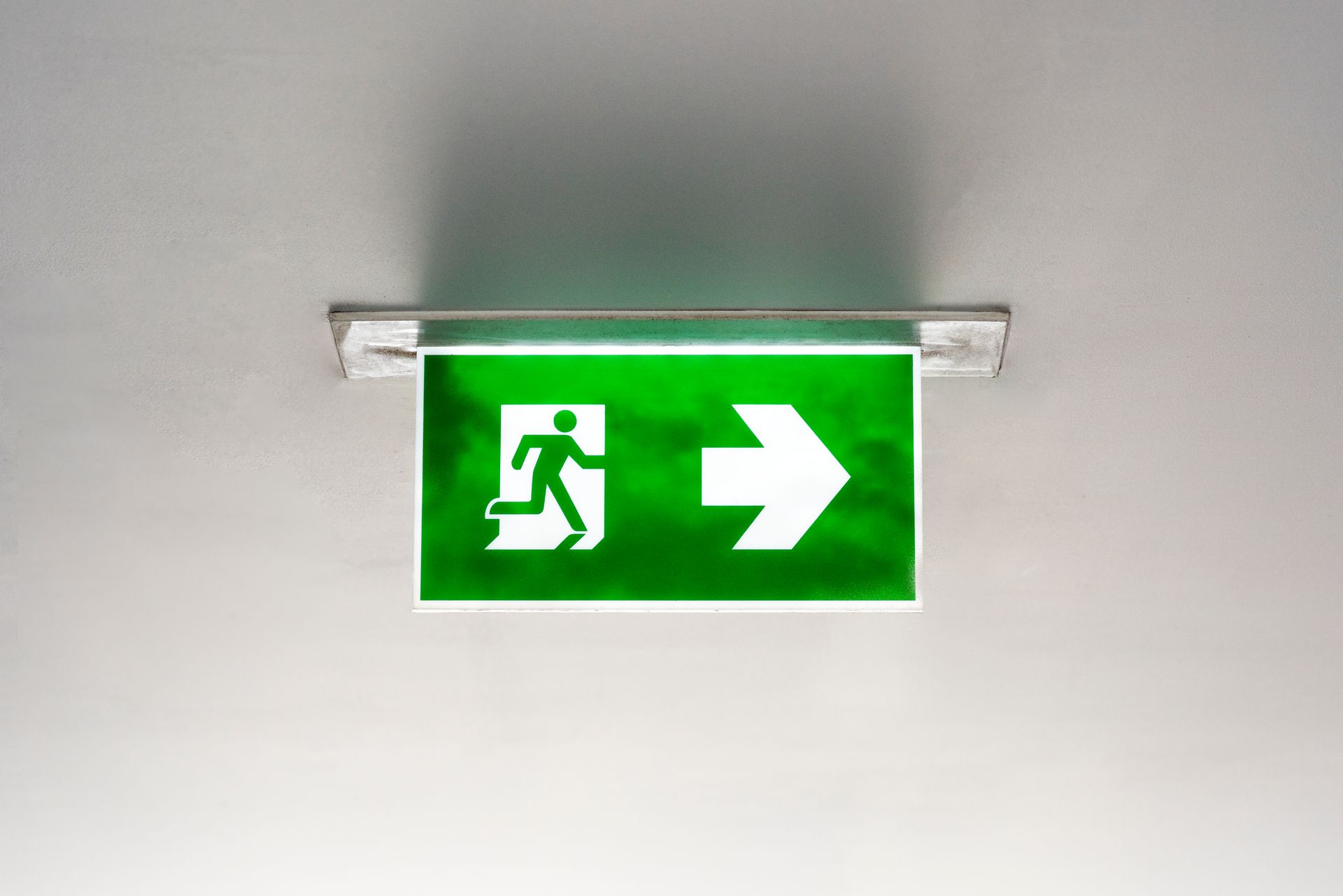 Panneau de sortie vert lumineux représentant une personne qui court et une flèche pointant vers la droite.