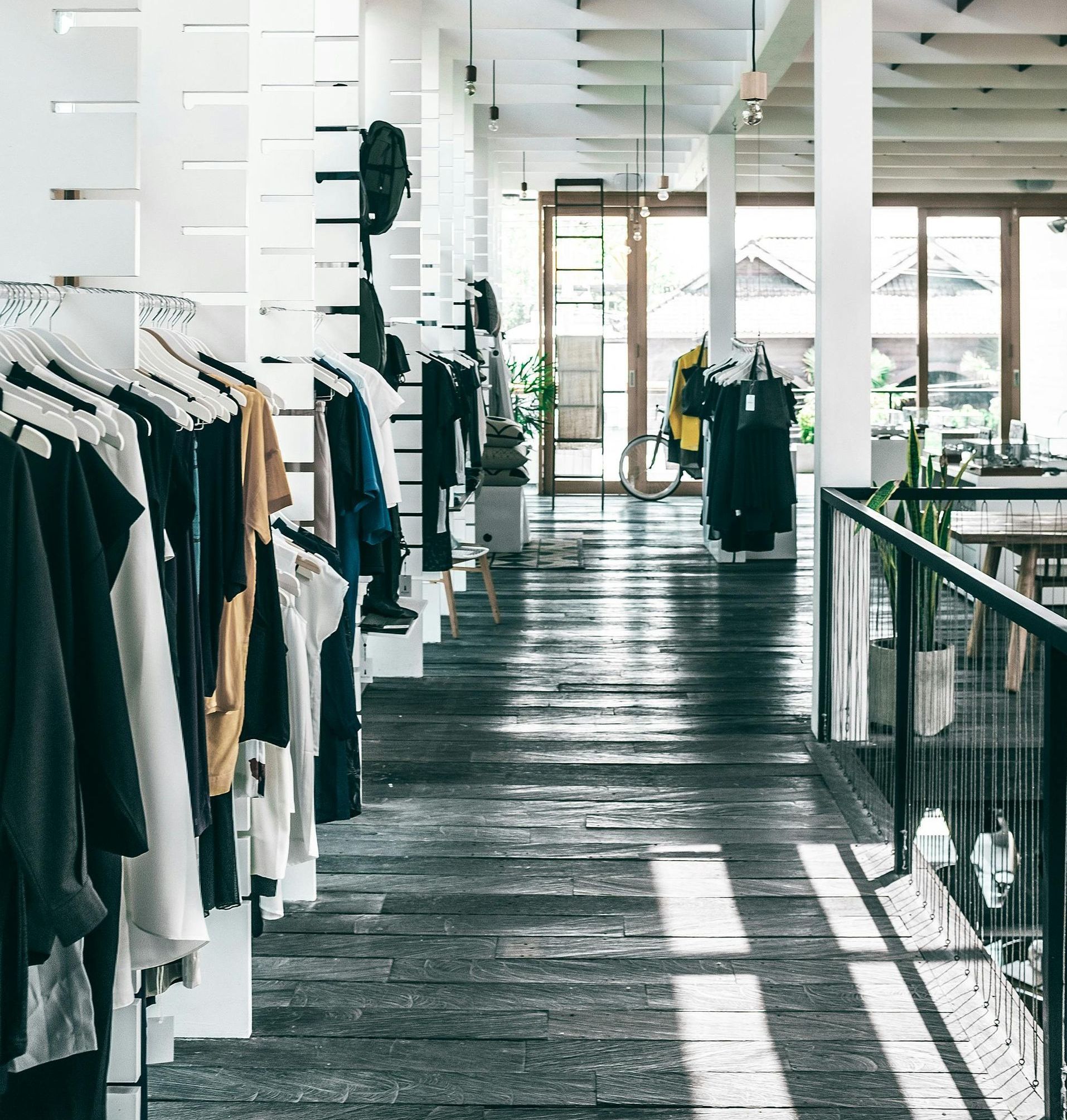 Intérieur d'un magasin de vêtements avec portants, parquet et grandes fenêtres.