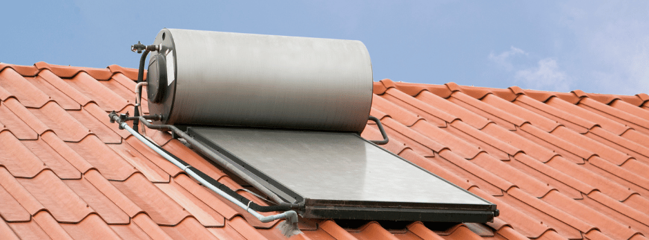 A solar water heater is sitting on top of a red tiled roof.