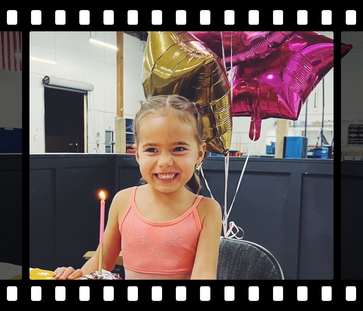 A little girl is sitting at a table with balloons and a candle.