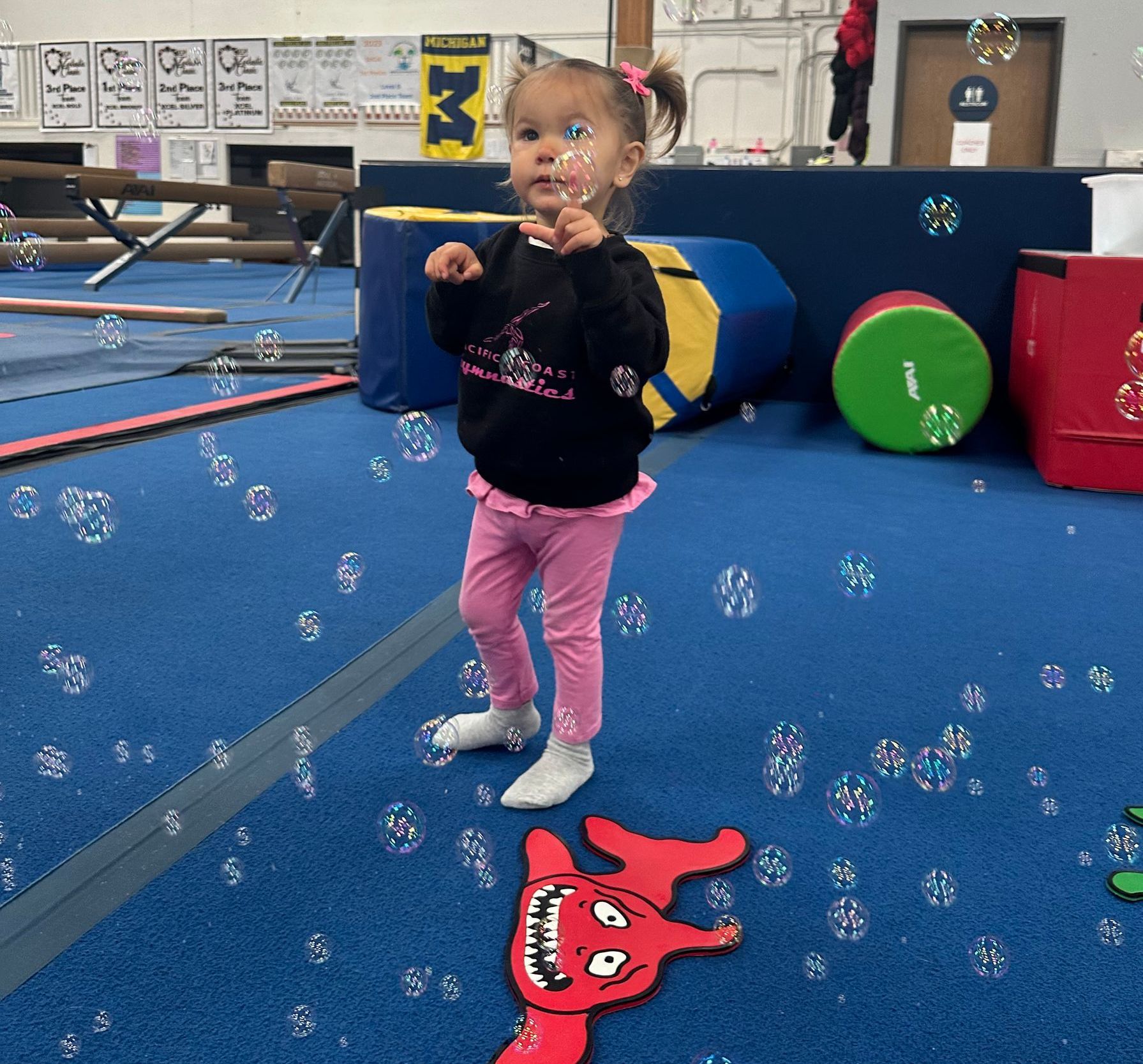 A little girl is blowing soap bubbles in a gym