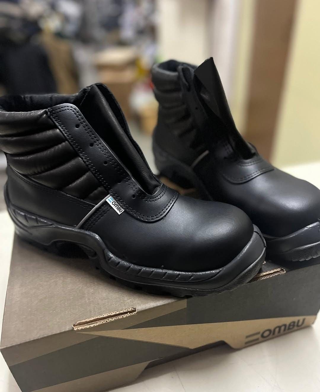 Botas de trabajo negras con cordones sobre una caja de zapatos en un entorno de tienda.