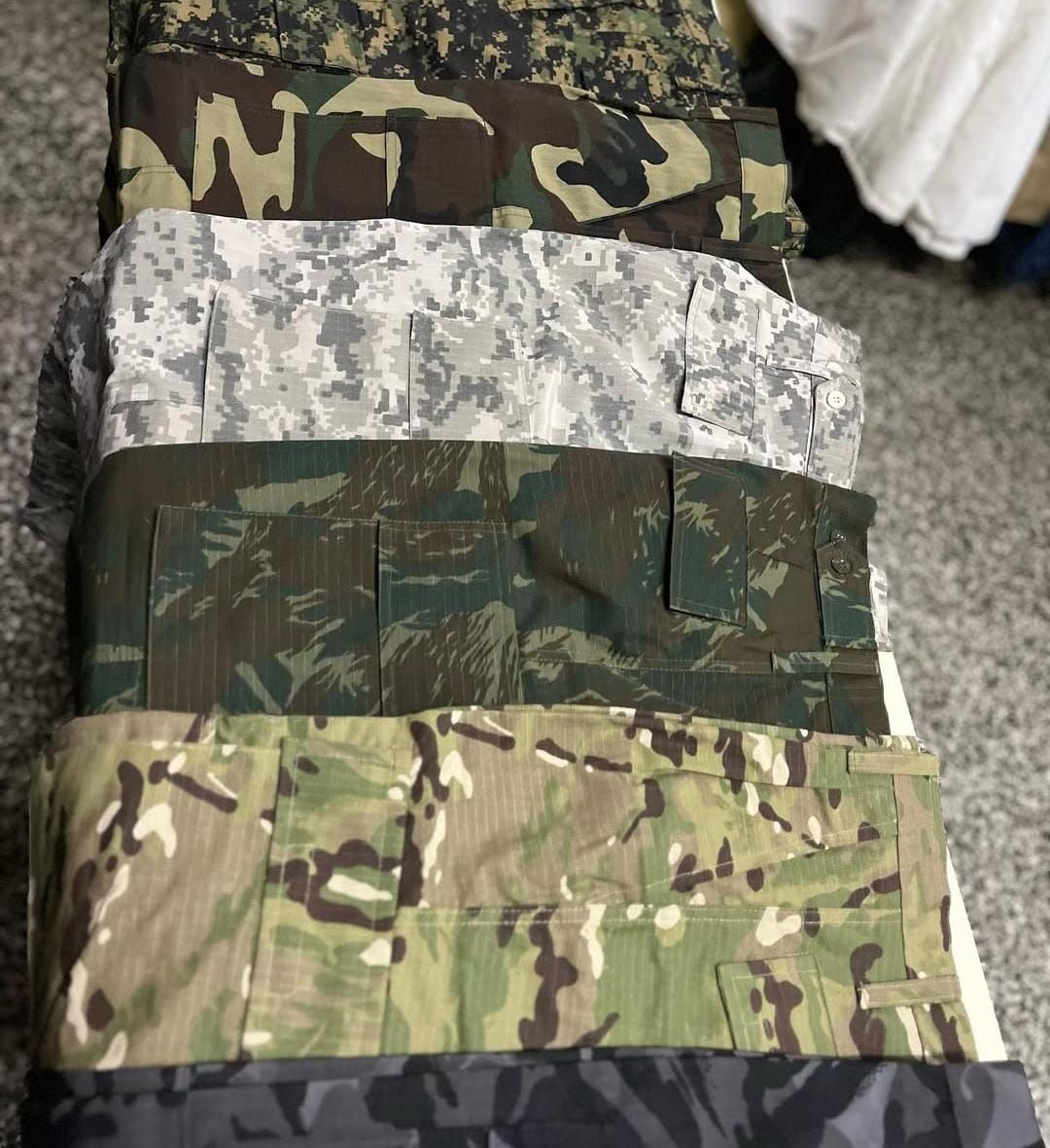 Muestras de tela de camuflaje apiladas en estampados verdes, beige, grises y negros sobre una mesa.