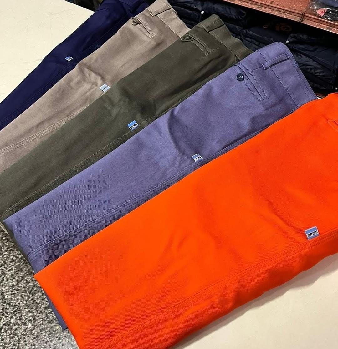 Pantalones doblados de color azul marino, caqui, verde oliva, lavanda y naranja brillante, dispuestos en diagonal sobre una mesa.