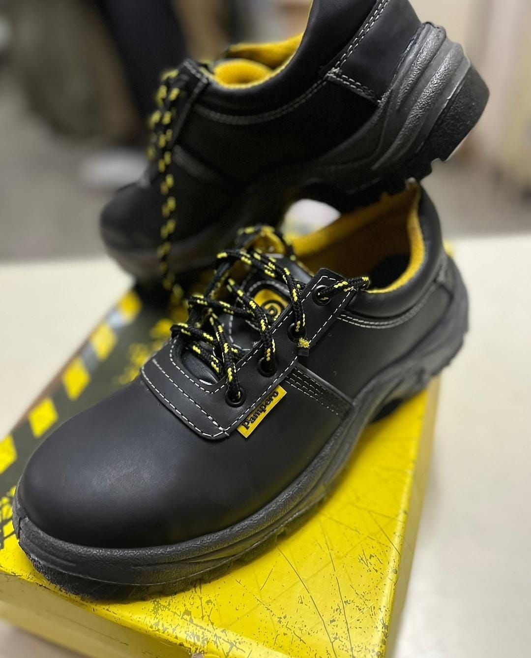 Zapatos de trabajo negros con detalles amarillos expuestos sobre una superficie amarilla.