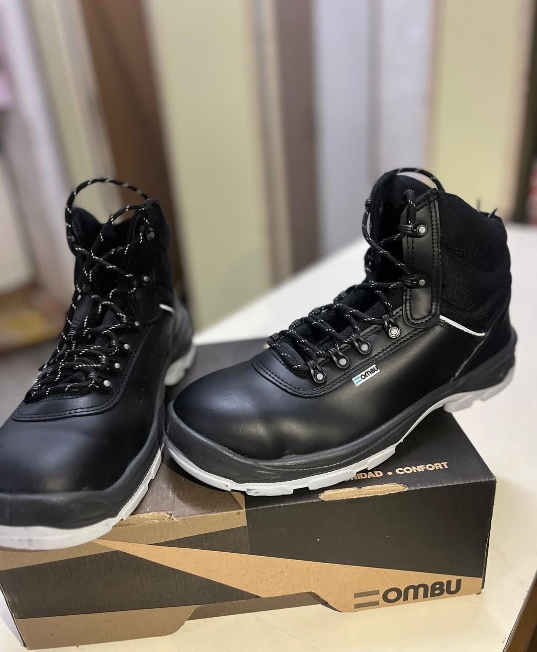 Botas negras de caña alta sobre una caja de zapatos, mostradas una al lado de la otra en interiores.