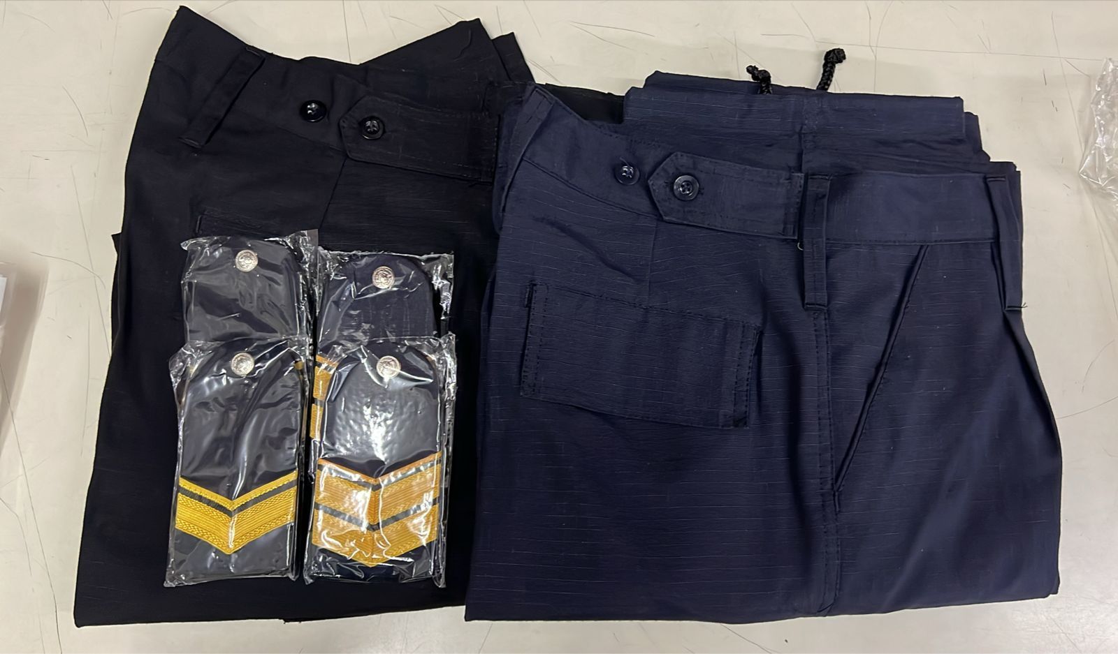 Dos pantalones azul marino doblados con un pequeño accesorio empaquetado encima de uno de ellos.