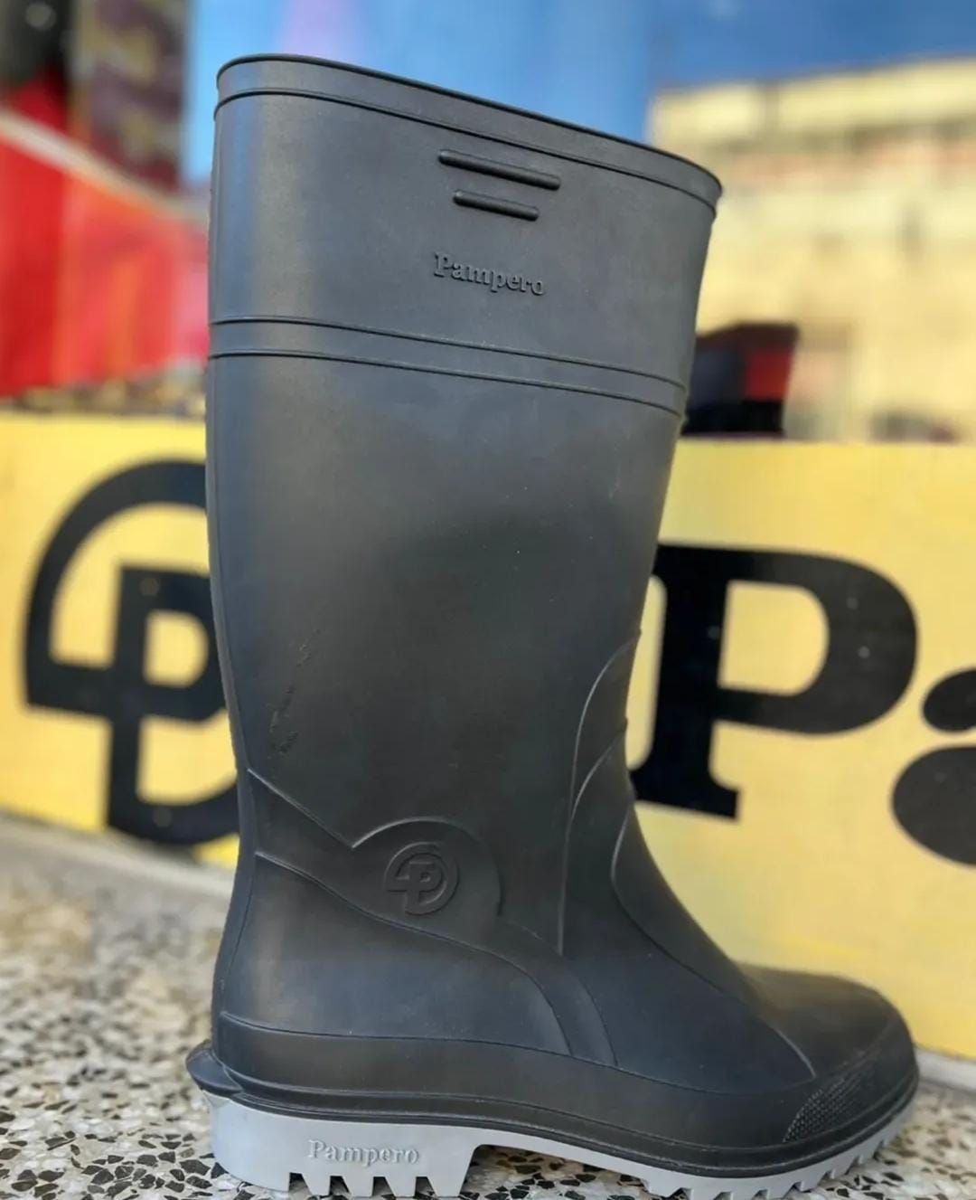 Una bota de trabajo de goma negra está de pie sobre una encimera, con un fondo difuminado en amarillo y negro.