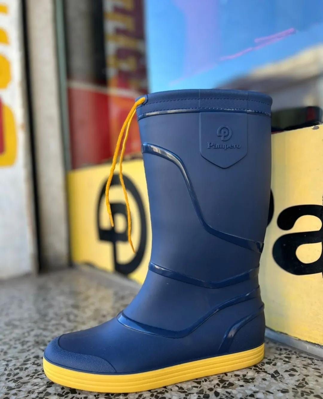 Bota de lluvia azul con suela amarilla expuesta al aire libre en el escalón de una tienda.