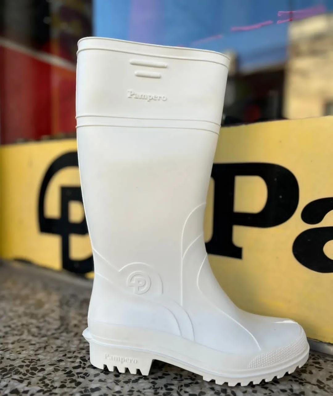 Una bota de lluvia blanca hasta la rodilla expuesta en la acera frente a un cartel amarillo.