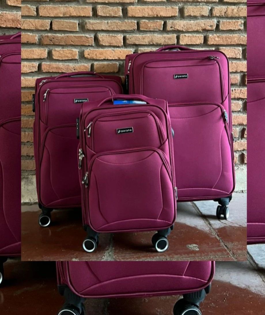 Tres maletas con ruedas de color burdeos expuestas frente a una pared de ladrillos.