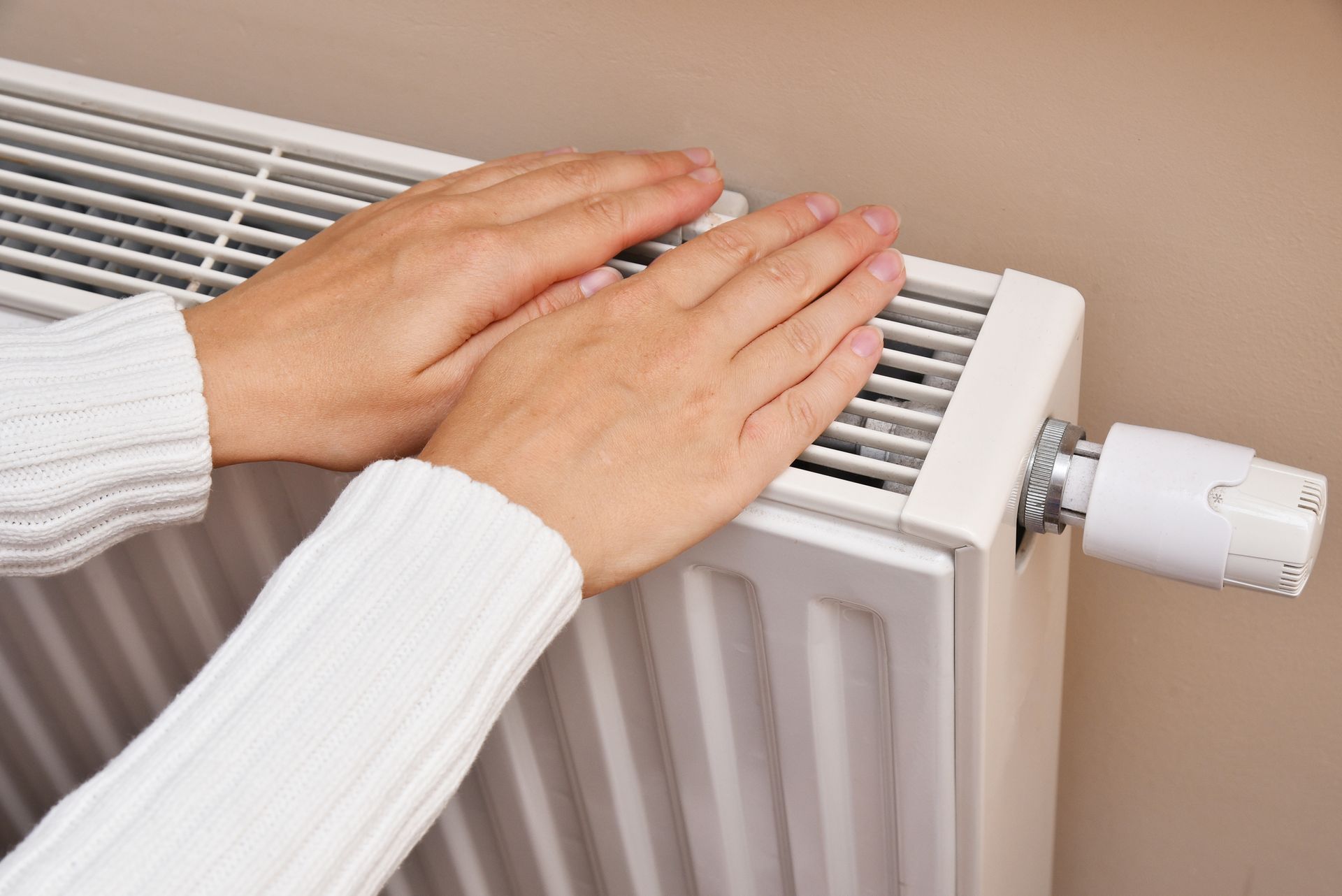 A woman warms her hands by the Heater Radiator