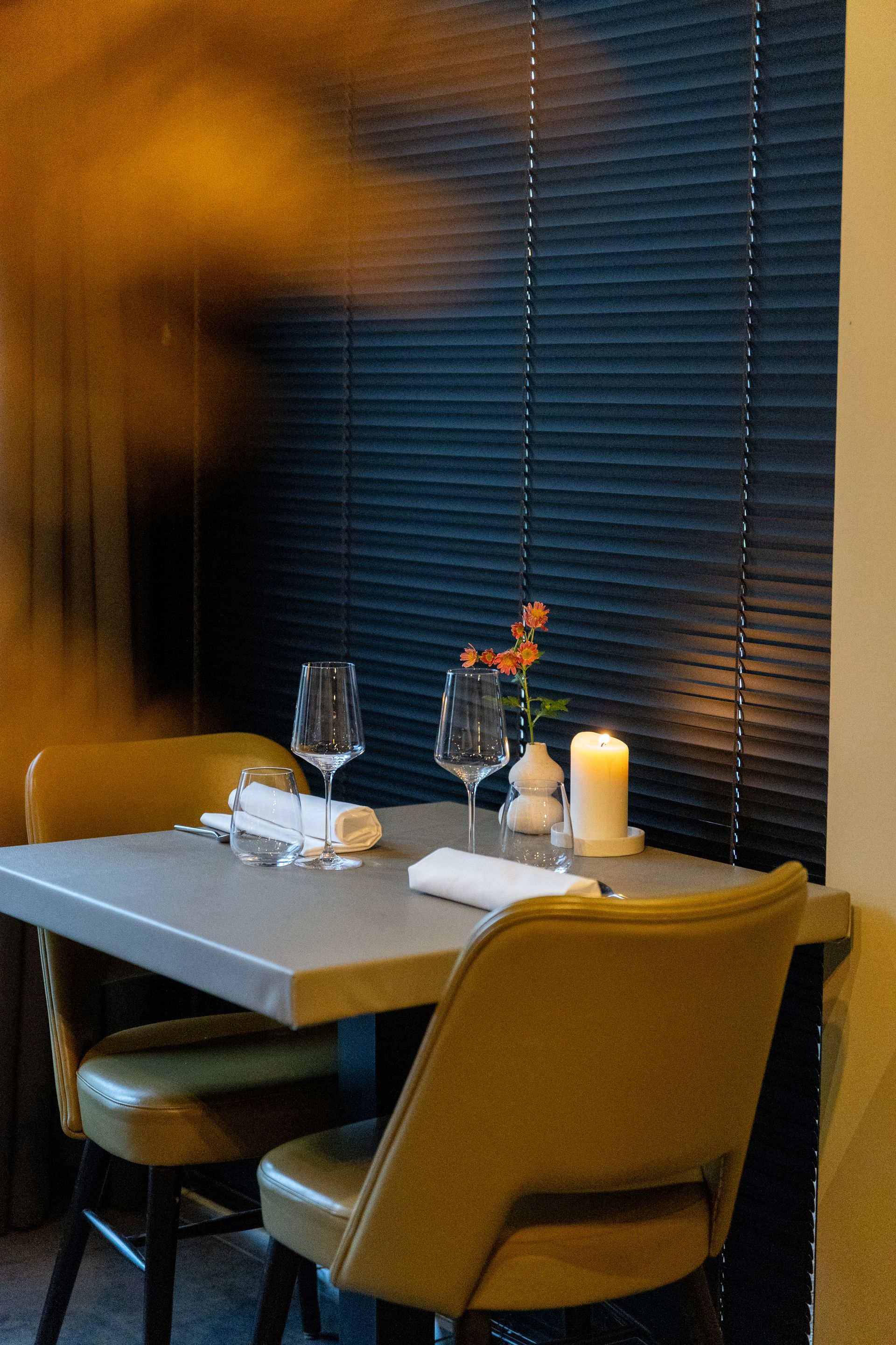 Een tafel gedekt voor twee in een restaurant: twee stoelen, wijnglazen, een kaars, bloemen en een servet.
