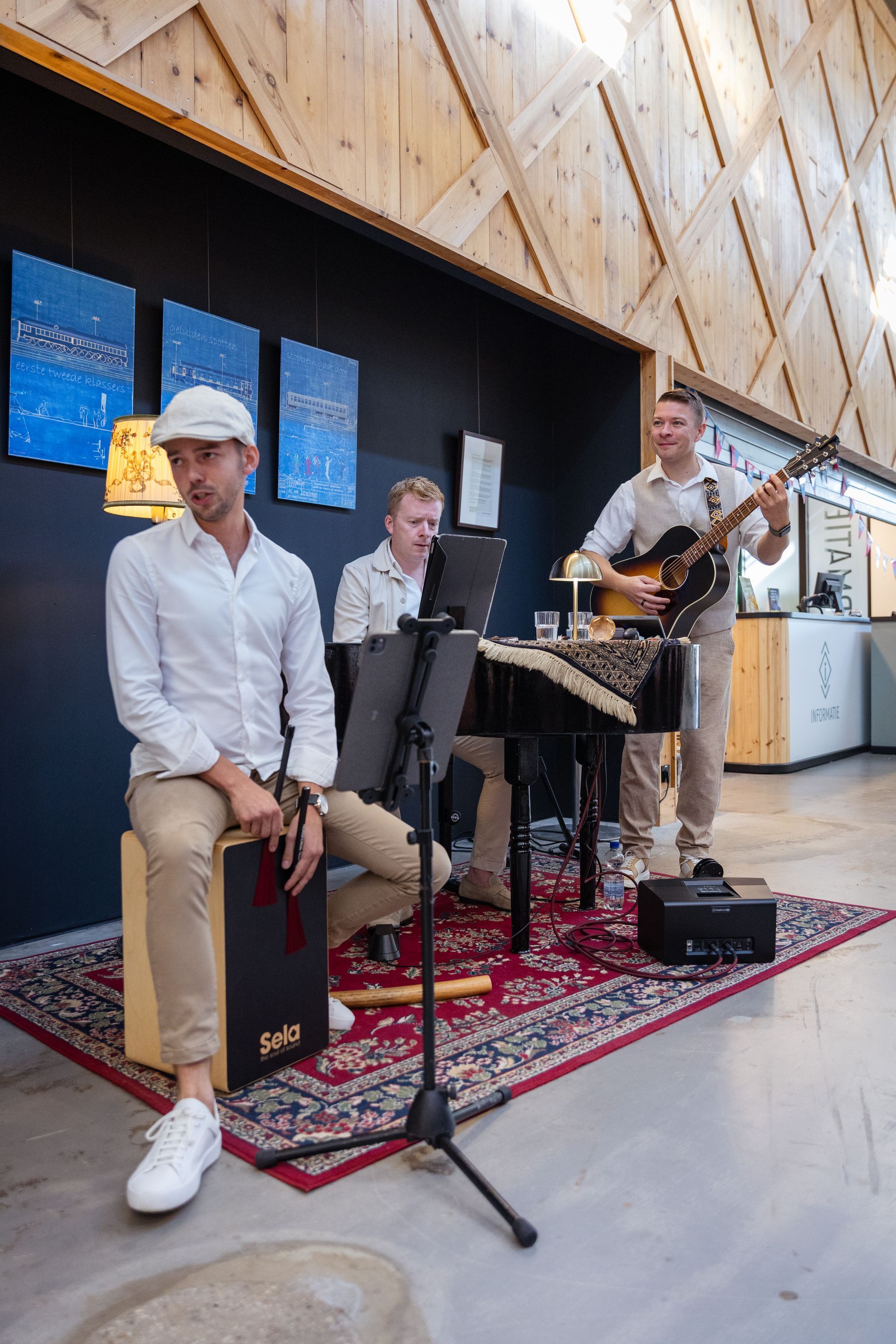 Een band die binnen optreedt: een percussionist, een toetsenist en een gitarist op een tapijt met een patroon.