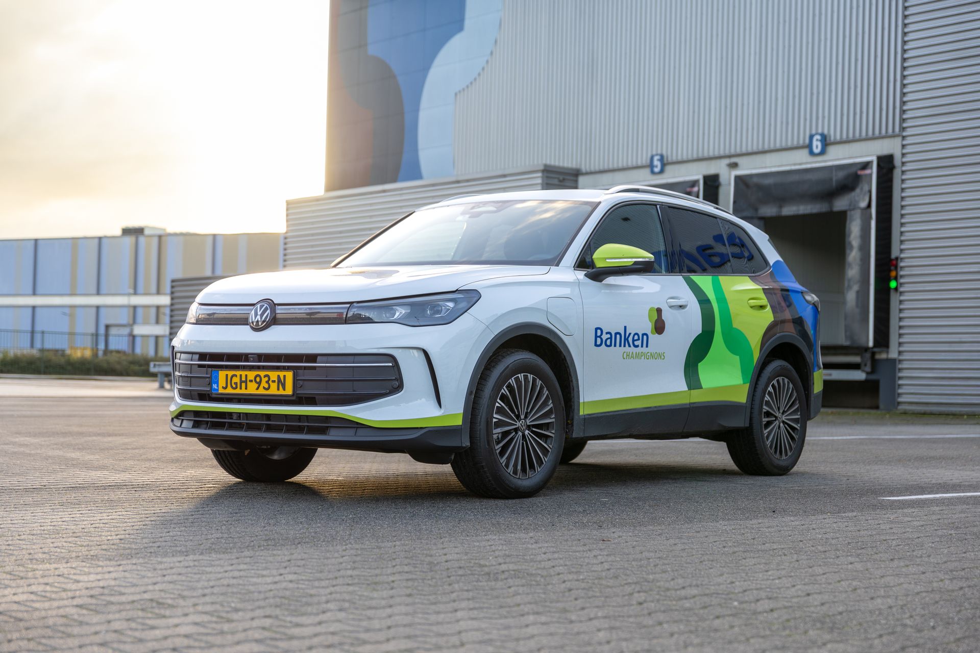 Witte SUV met bedrijfslogo geparkeerd nabij een industriegebouw.