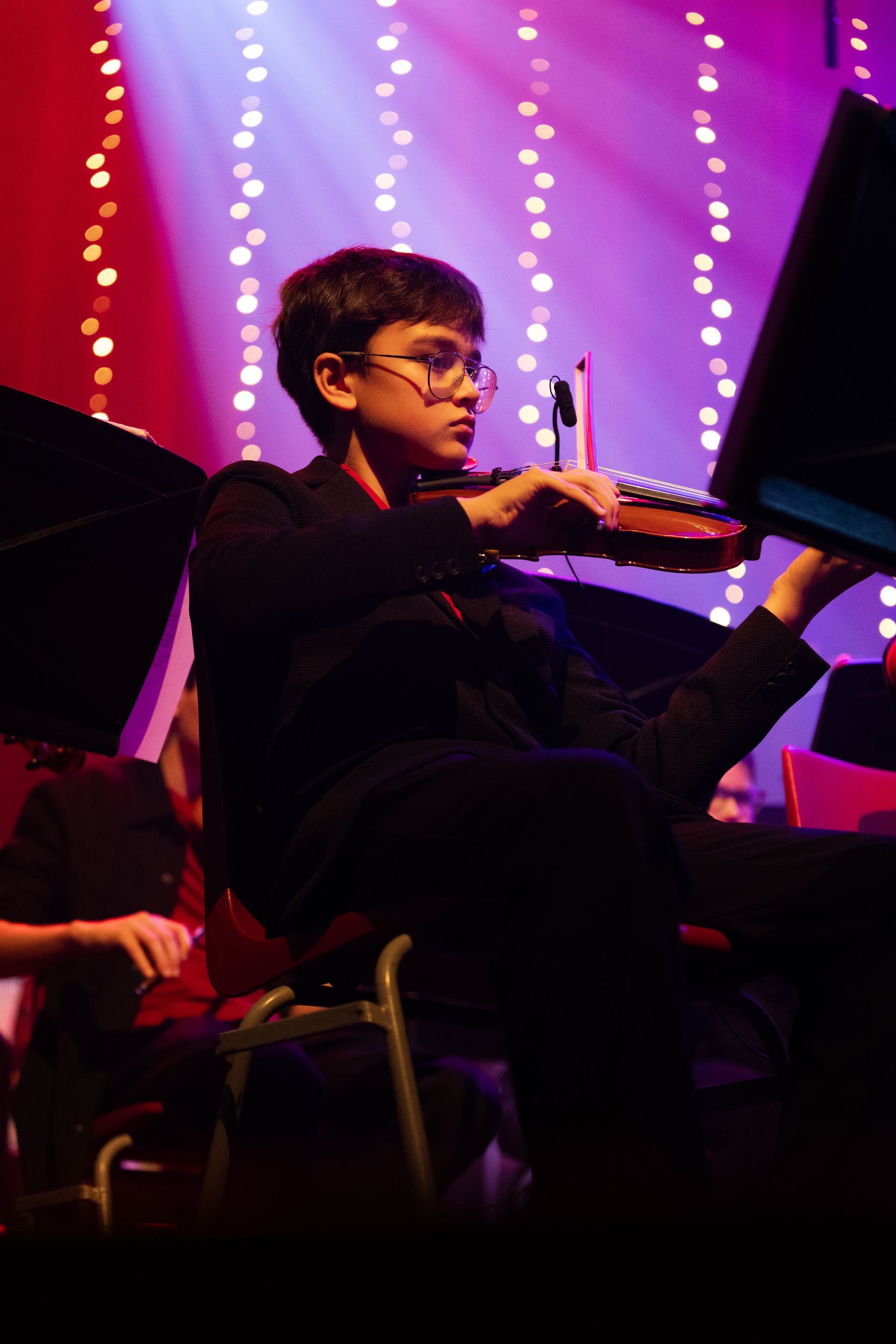 Een persoon die viool speelt in een orkest, het podium verlicht met lichtsnoeren.