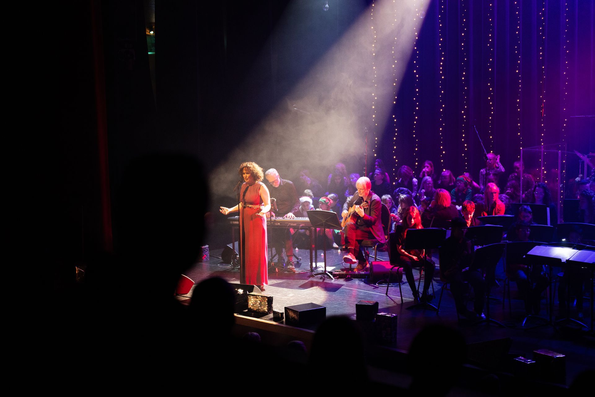 Vrouw in rode jurk zingt op het podium met orkest en koor, in de schijnwerpers.