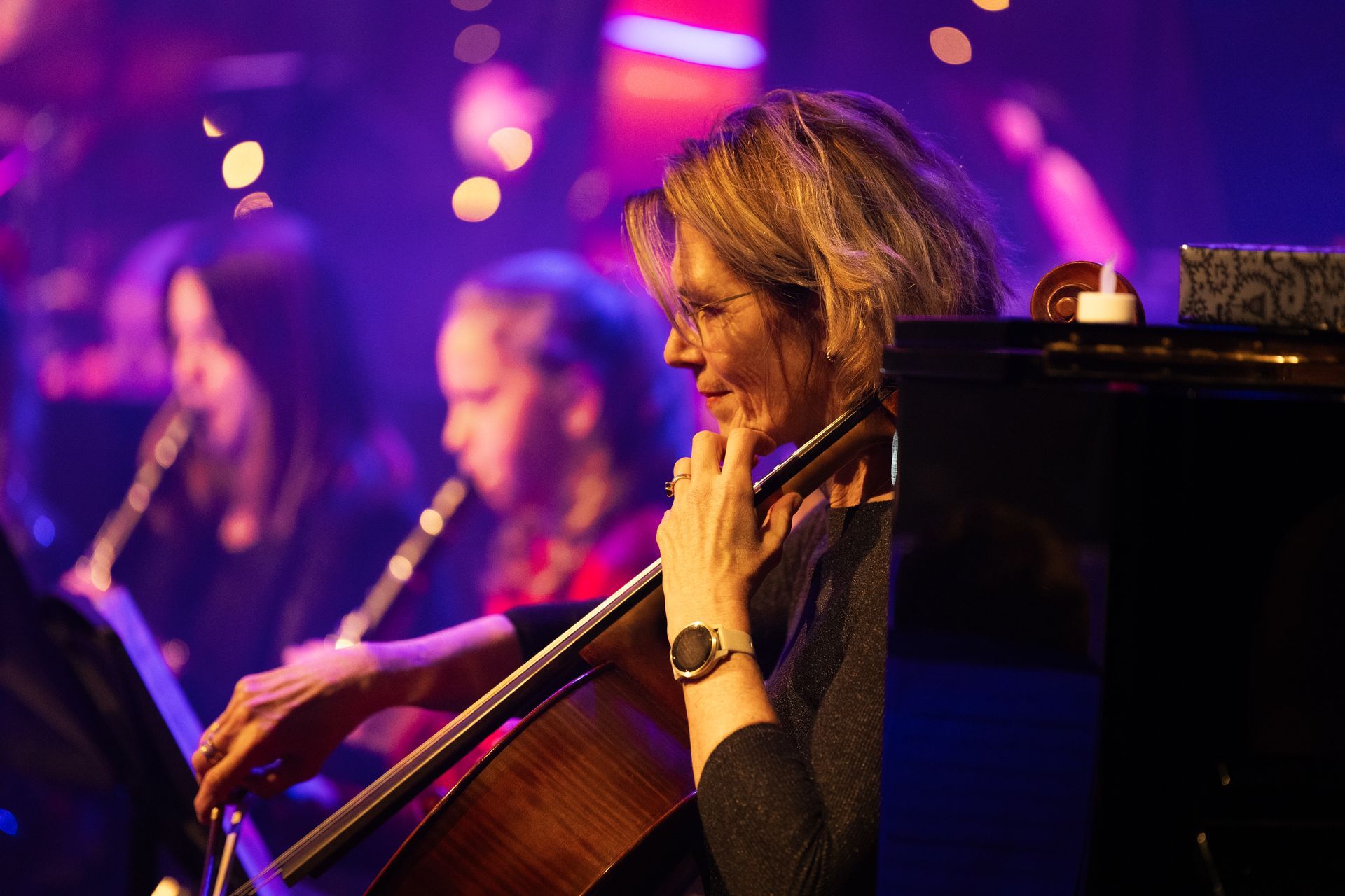 Vrouw die cello speelt in een orkest, verlicht door podiumverlichting.