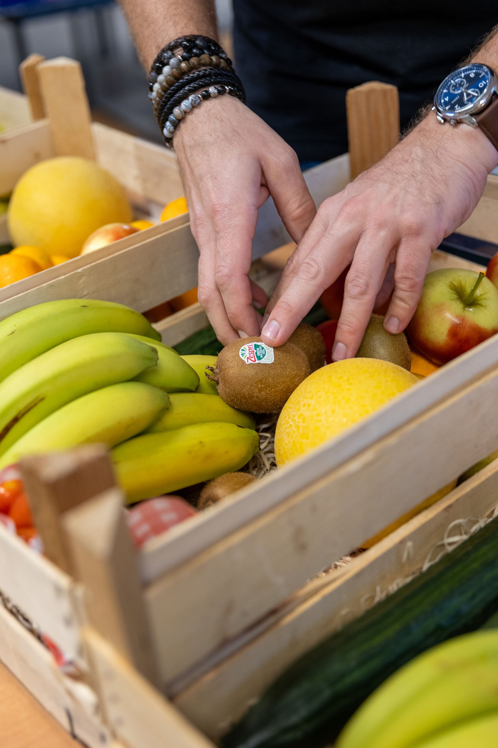 Iemand sorteert fruit zoals bananen, kiwi's en citroenen in houten kratten.