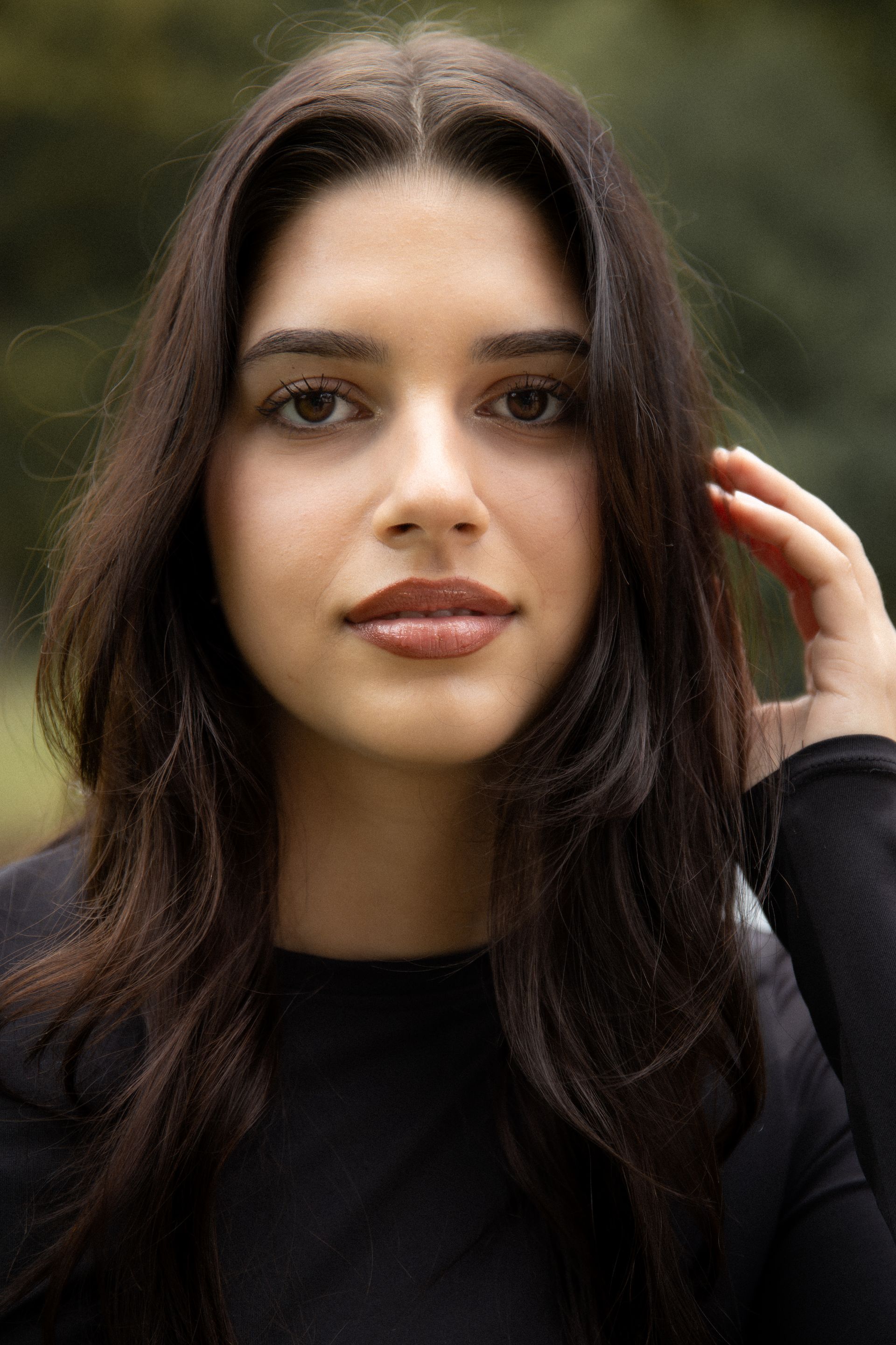 Vrouw met lang donker haar, gekleed in een zwarte top, glimlacht lichtjes, buiten.