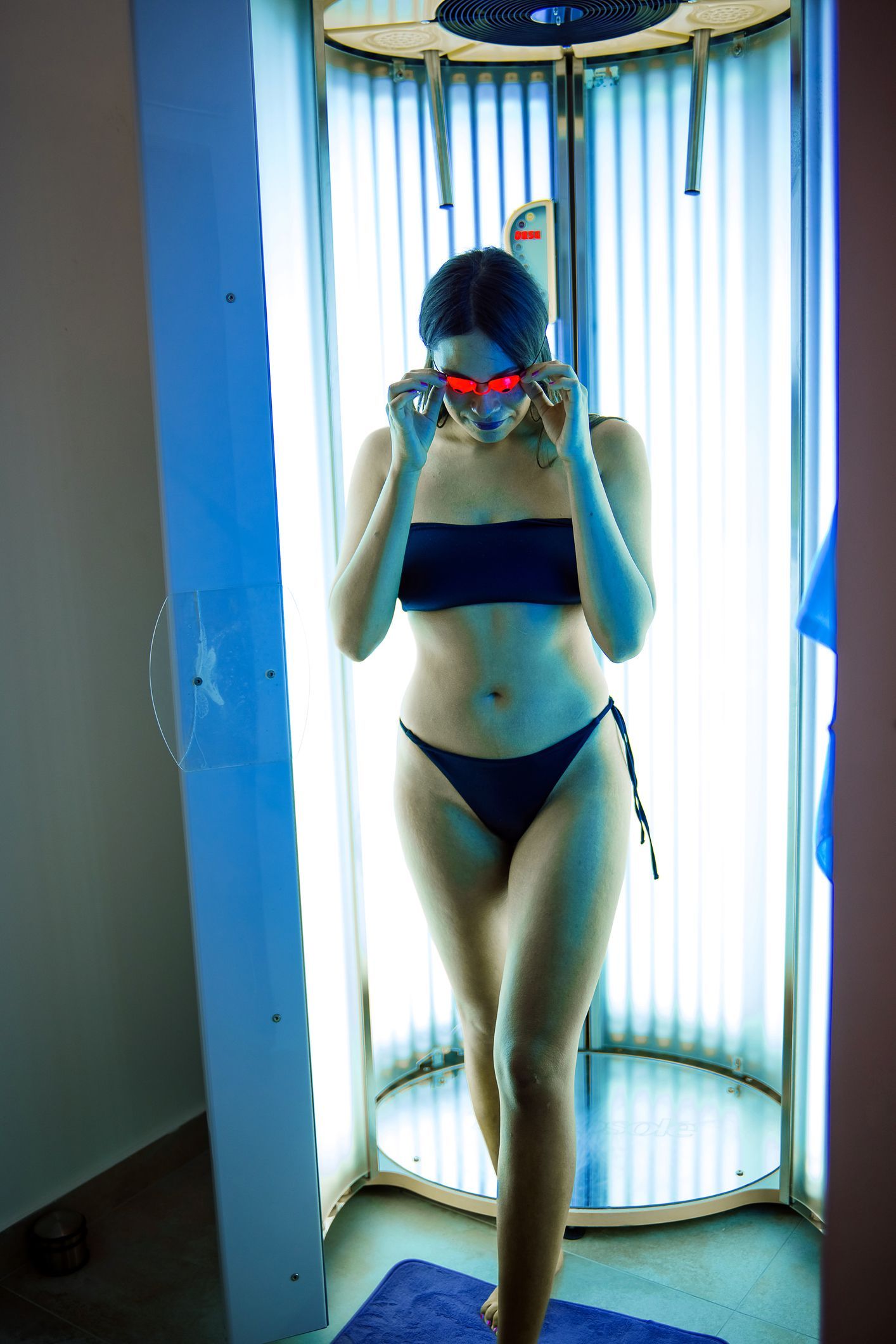 A woman in a bikini is standing in a tanning booth.