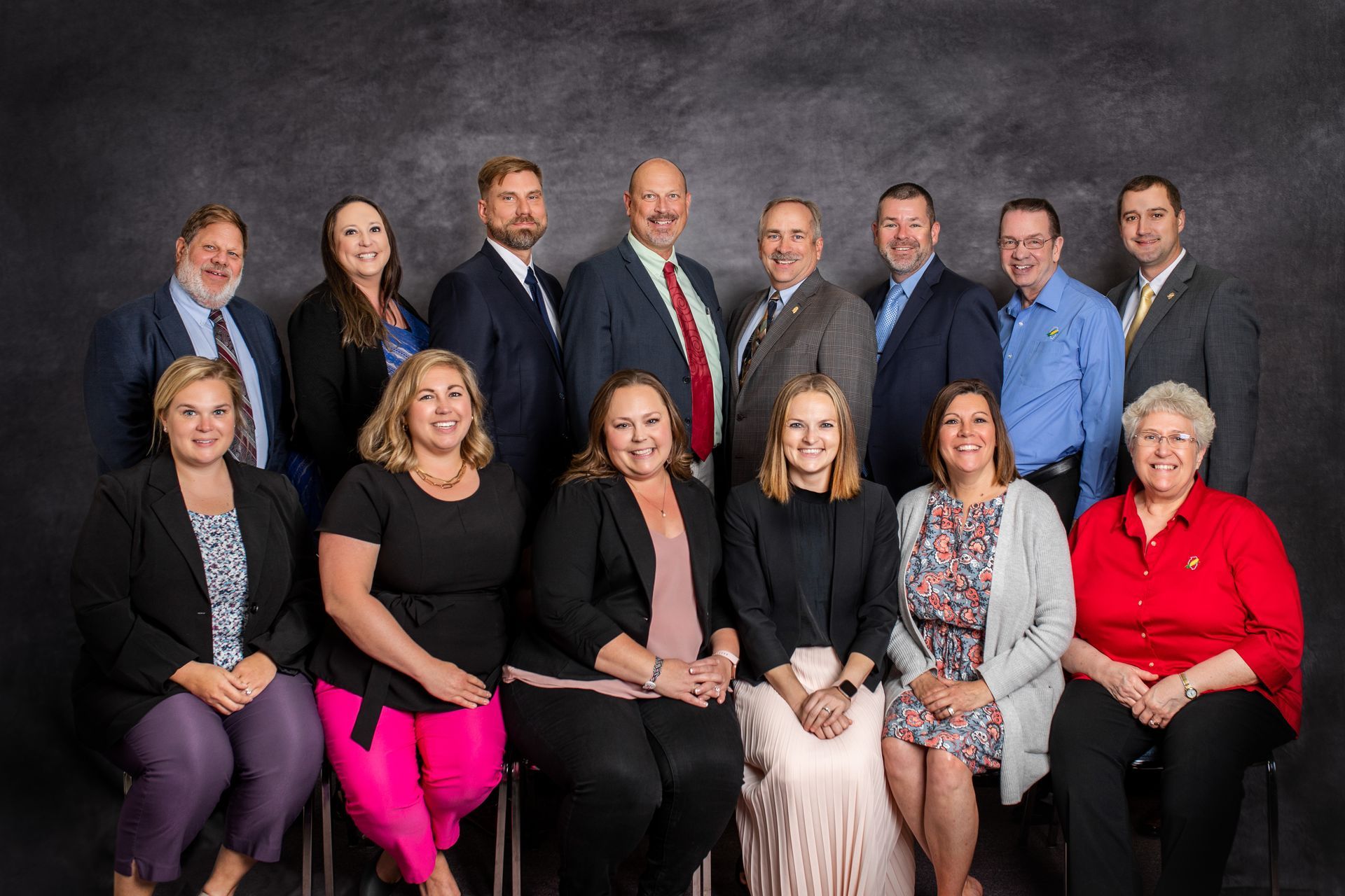 Group photo of 13 people in business attire posing in front of a dark gray backdrop.