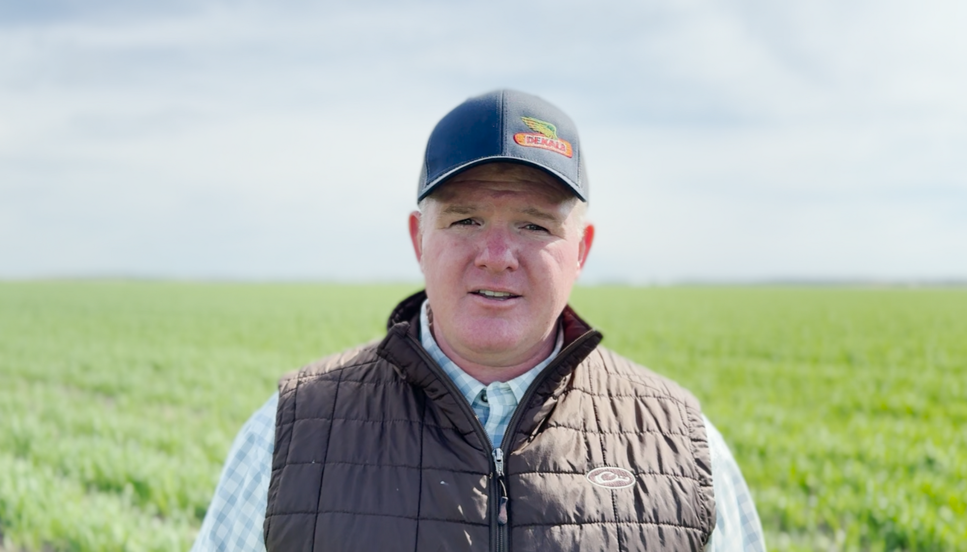 A man wearing a hat and vest is standing in a field.