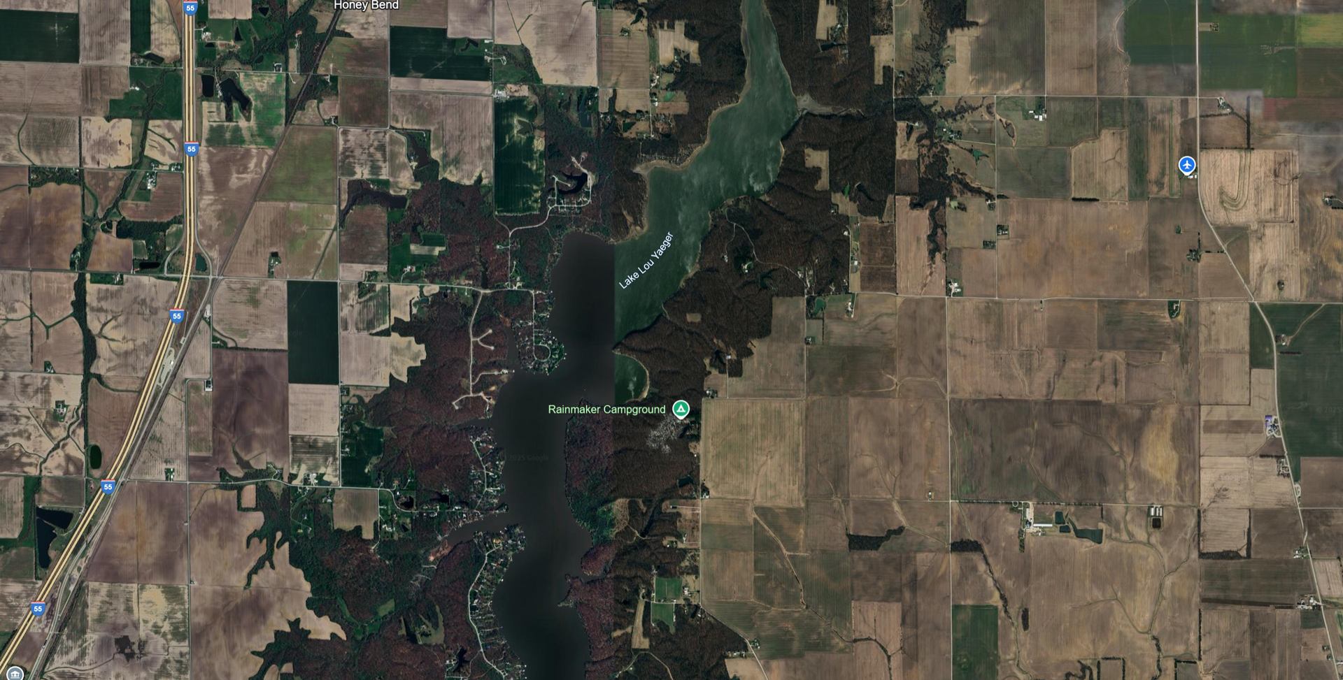 Aerial view of a lake surrounded by fields and trees, with roads visible.