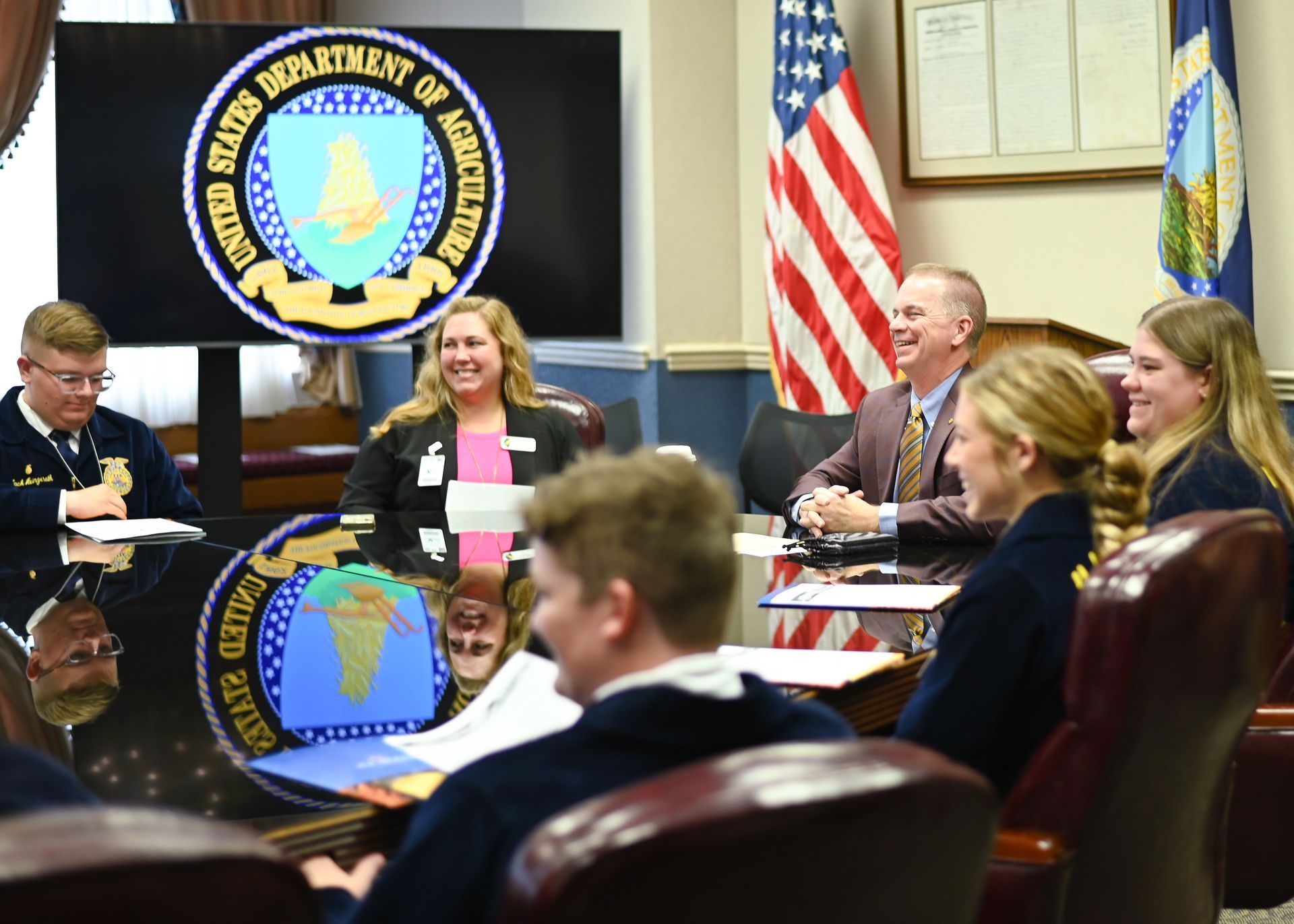 A group meets in a U.S. Department of Agriculture office. Smiling people sit around a table.