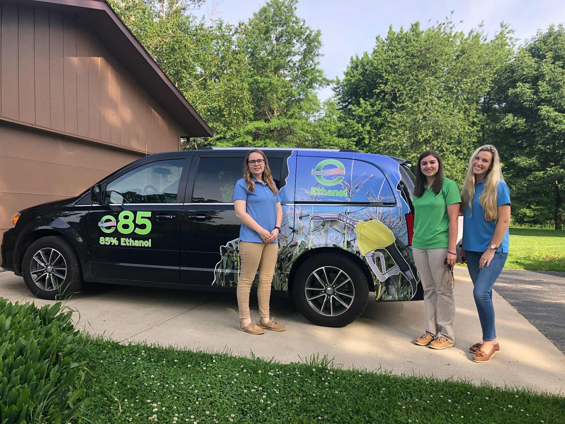 Three people stand by a black van with green and blue artwork. The van says