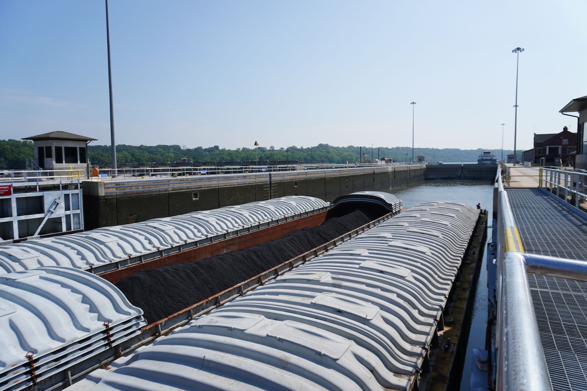 Cargo containers lined up at a port beside a canal, under a bright sky