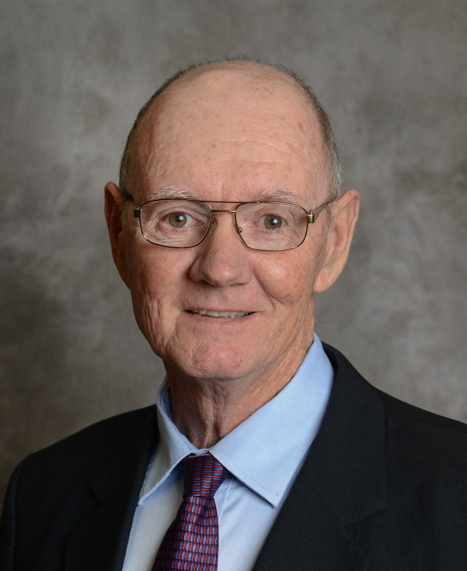 Older man with glasses, smiling, wearing a suit and tie.