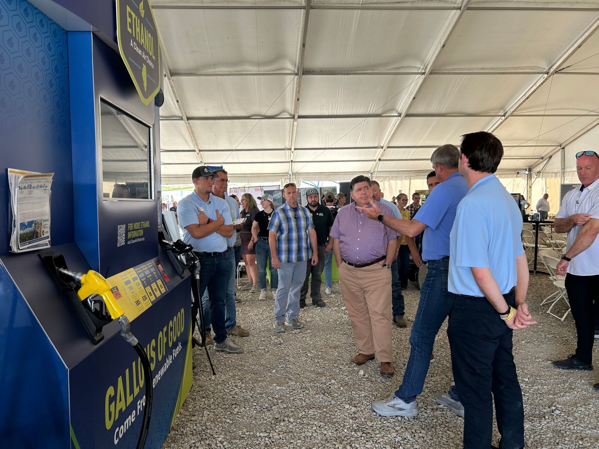 People gathered around a blue fuel pump, possibly at an event. Some are looking, talking, and gesturing.