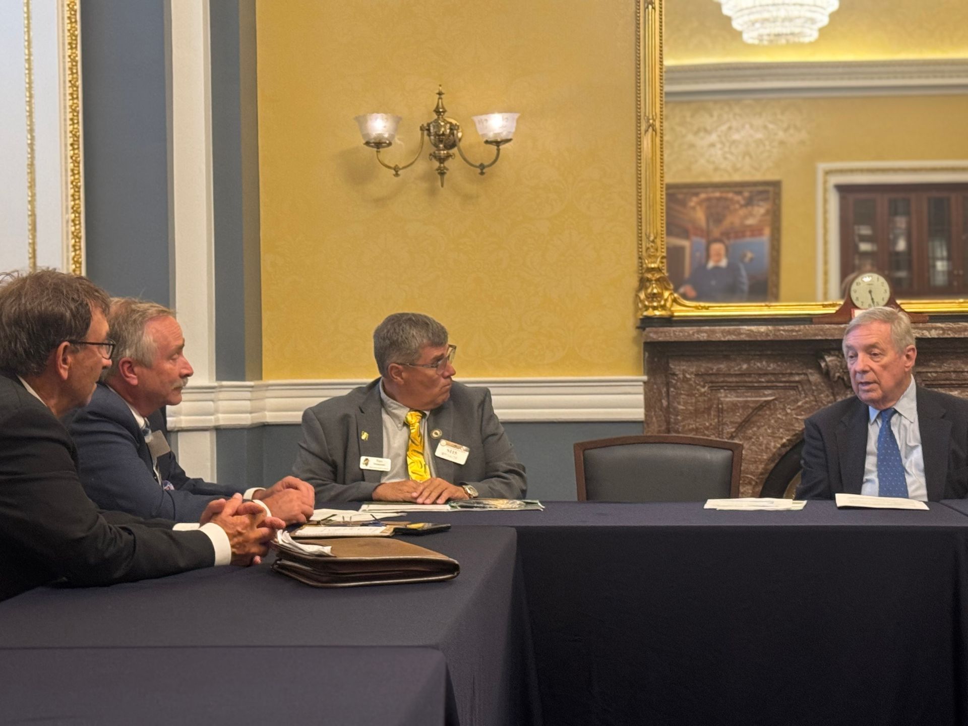 Men in suits at a table in a formal room, possibly a meeting or discussion in progress.
