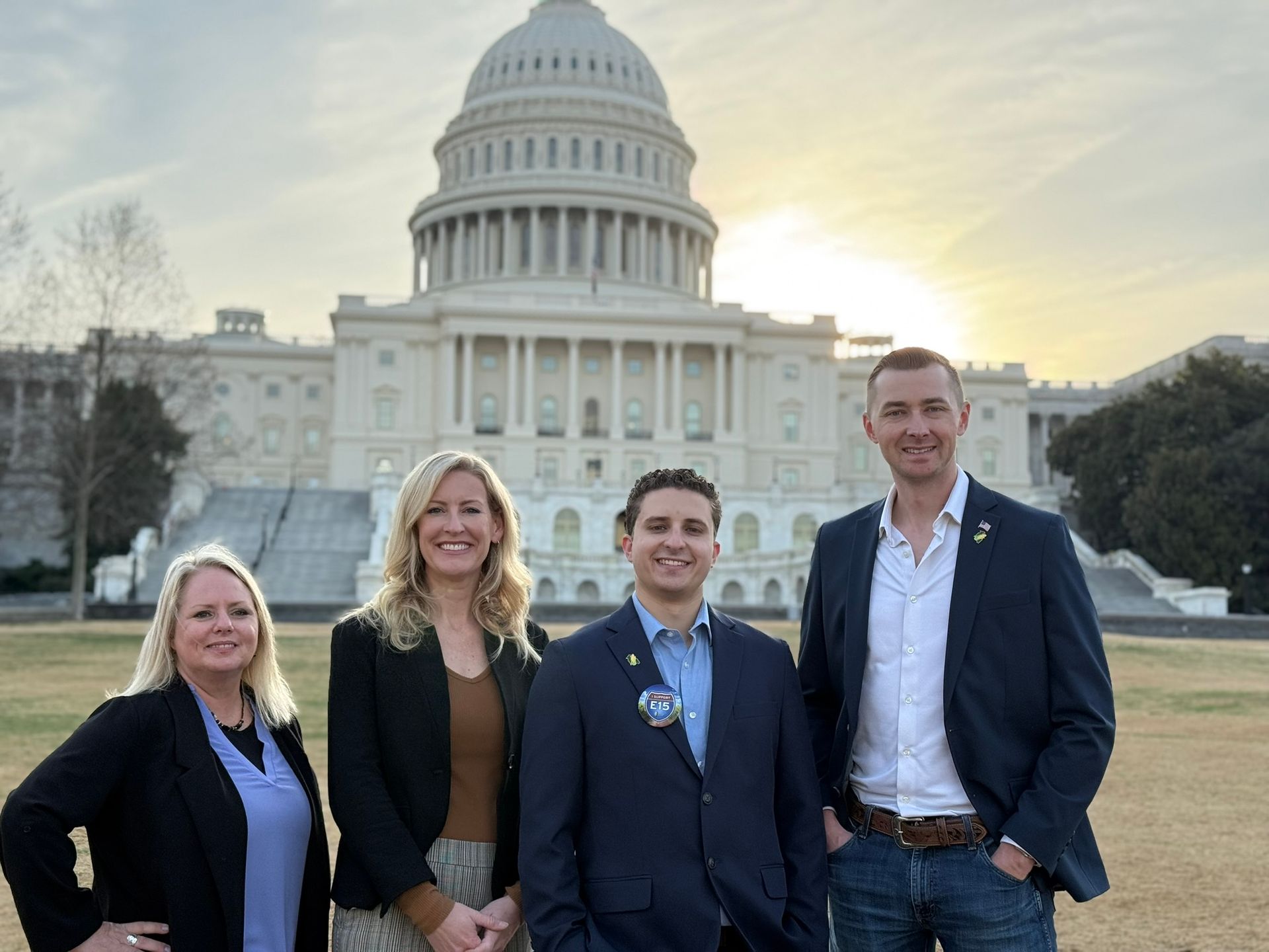 Four people in front of the U.S. Capitol building. They are smiling, wearing business attire, during the daytime.