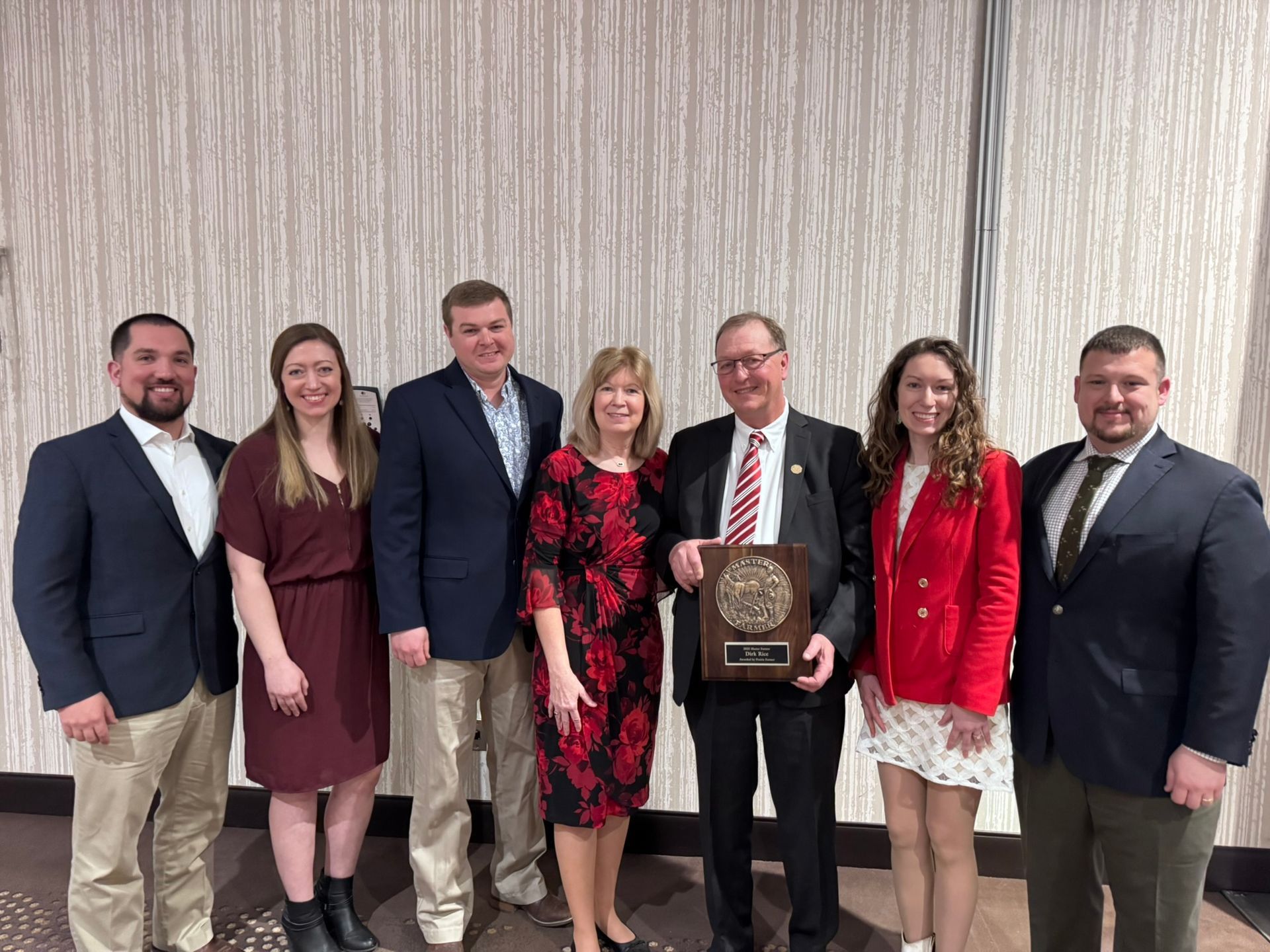 Group of seven people posing with an award in a formal setting.