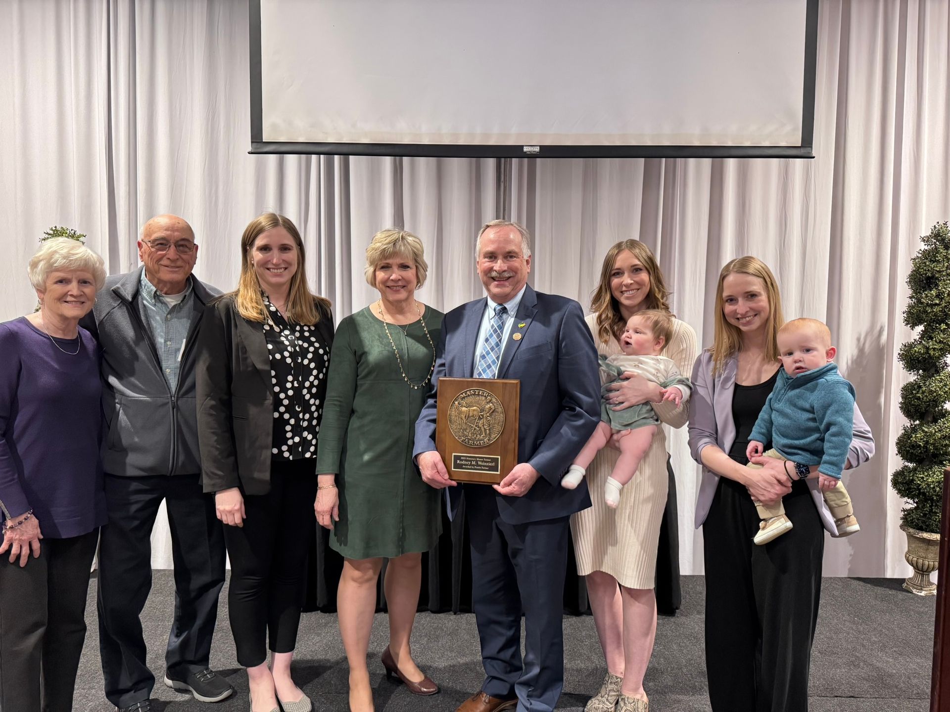 Group poses with plaque on stage; man holds plaque, others smile.