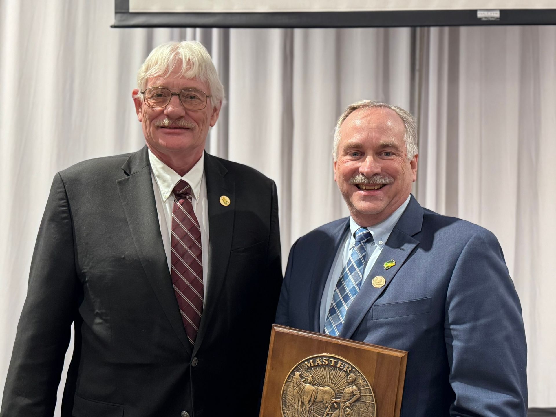 Two men in suits holding an award. One man is smiling and holding the plaque.