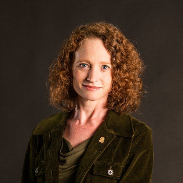 A woman with red curly hair is wearing a green jacket