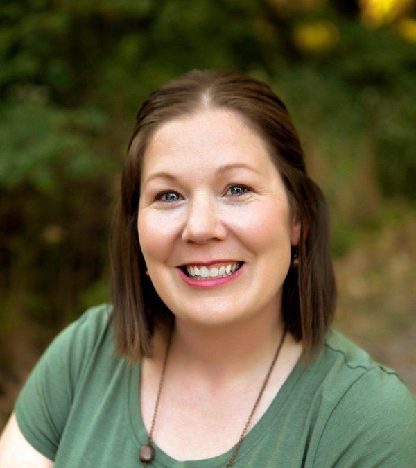 A woman in a green shirt is smiling for the camera.