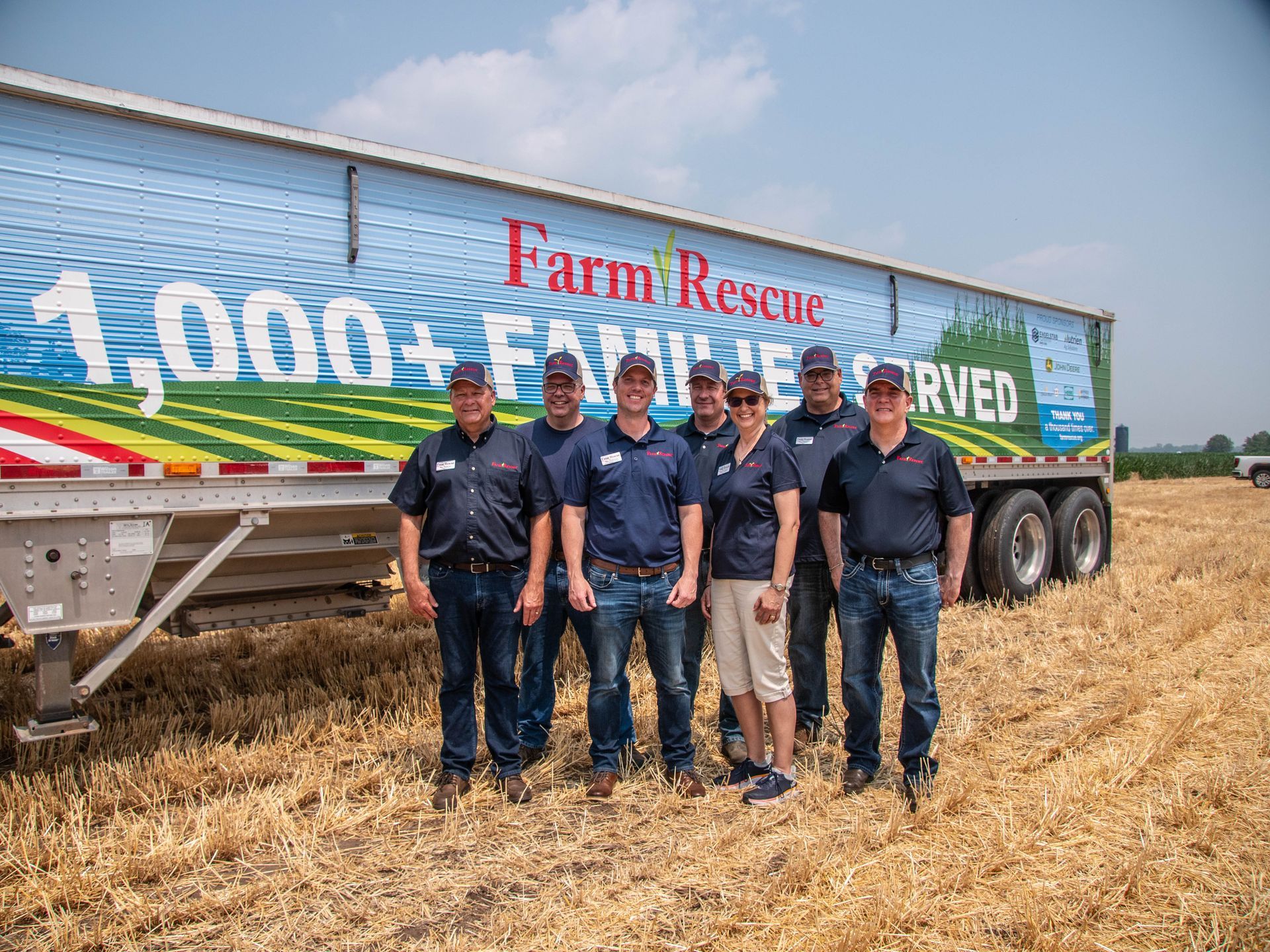 Group of people standing in front of a Farm Rescue trailer in a field, under a blue sky.